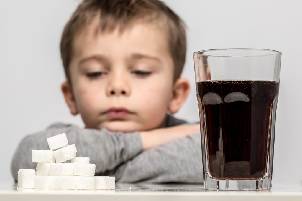 child staring at a glass of soda and a pile of sugar